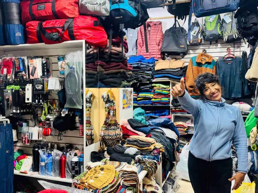 Alt Text: Frau im Second-Hand-Laden, umgeben von outdoor und Reisezubehör.