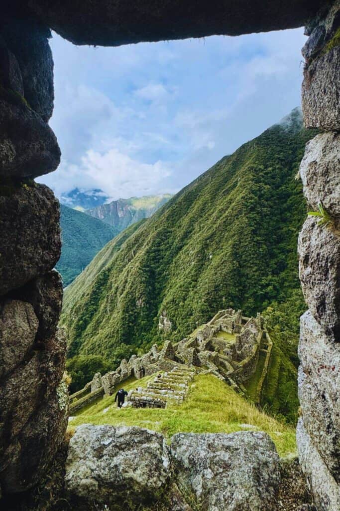 Beeindruckender Blick auf die Inka-Ruinen, umgeben von grünen Bergen, durch einen Felsenfensterrahmen betrachtet.