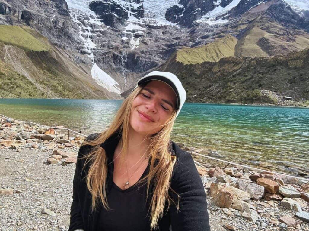 Frau entspannt an einem ruhigen Bergsee in Peru, umgeben von hohen Bergen und klarer Wasserlandschaft, ideal für Natur- und Outdoor-Liebhaber.