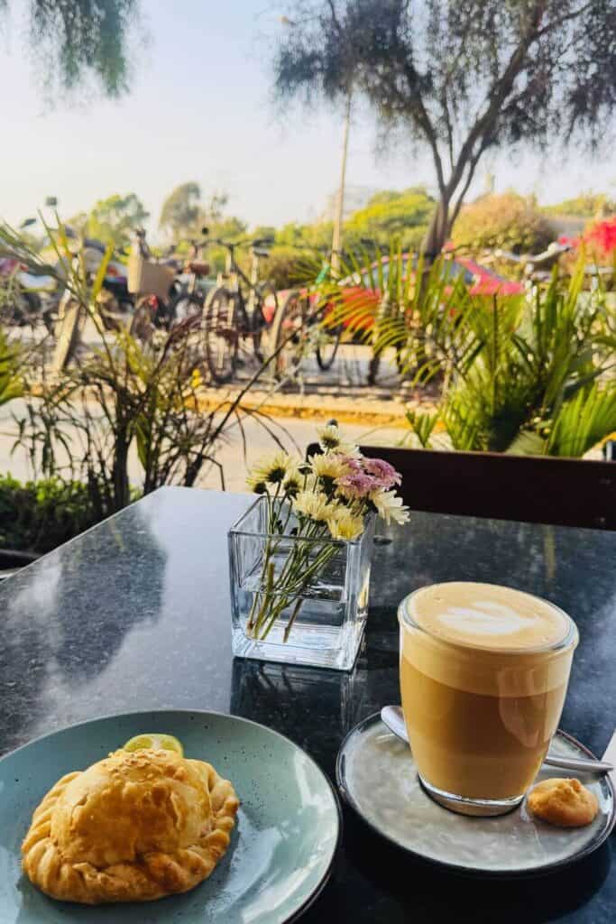 Einladendes Café mit Kuchen, Kaffee und Blumen im Außenbereich, entspannte Atmosphäre.