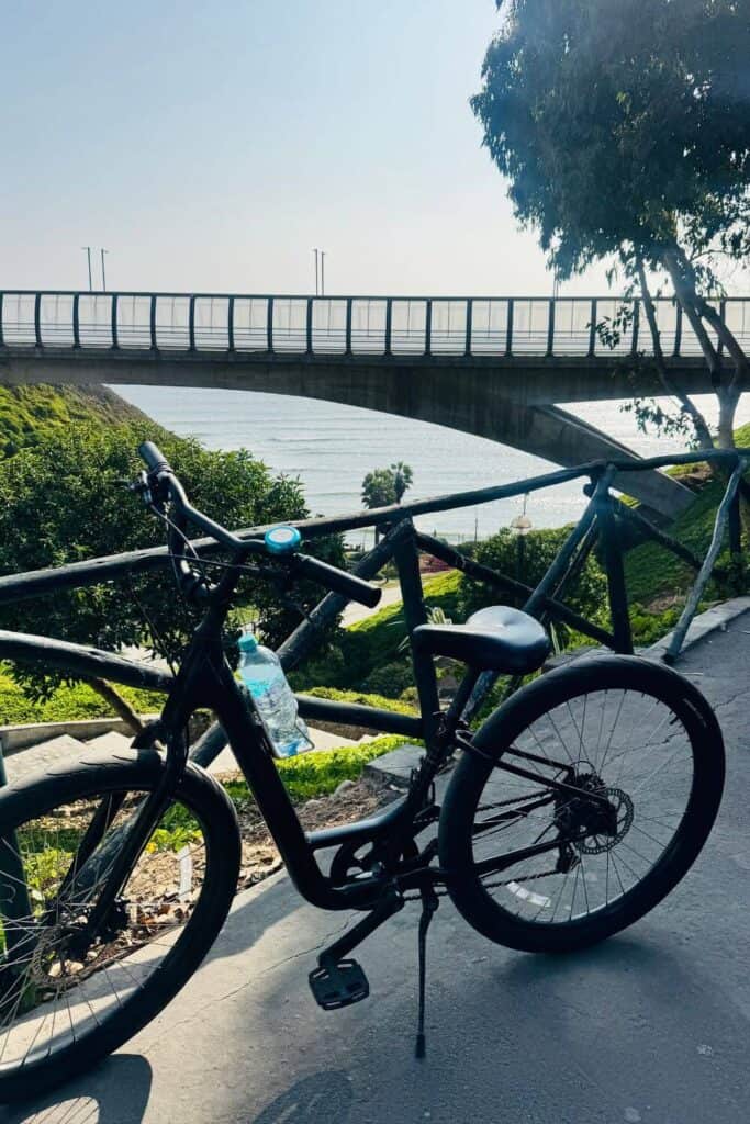 Rotes Mountainbike am Meer mit Brücke im Hintergrund.