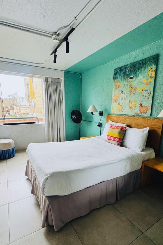 Bett in modernem Hotelzimmer mit buntem Wandbild und Stadtblick.