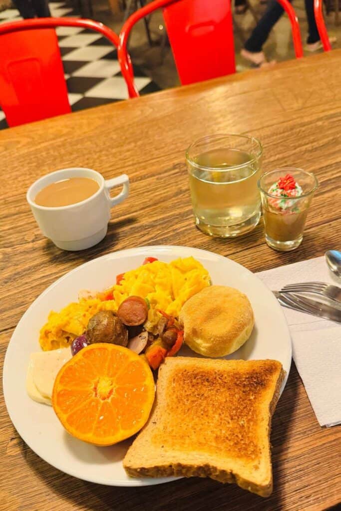 Frühstücksteller mit Orangenscheibe, Toast, Eierspeisen und Kaffee in gemütlichem Café.