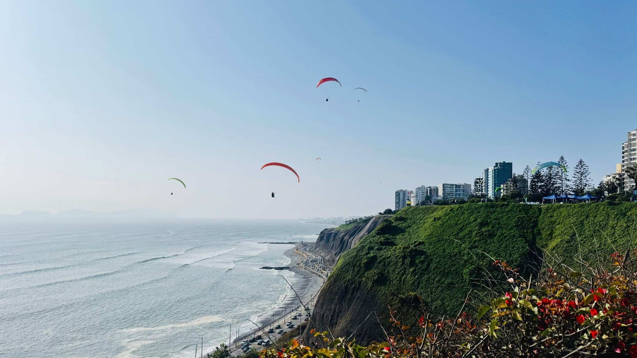 Lima_Peru_Guide_Paragliding_Meer_Sunset Paragliding über der Küste von Lima in Peru mit Hochhäusern und grünen Hügeln, sonniger Himmel, Meeresblick.
